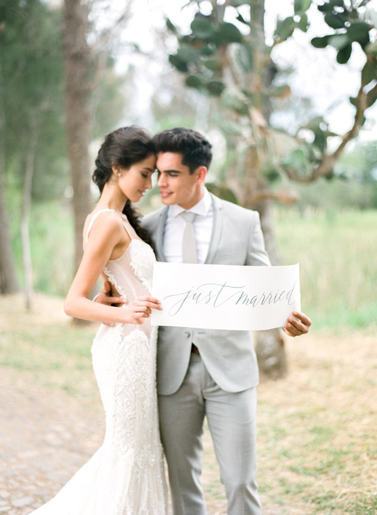 Groom and bride holding sign that say just married in calligraphy