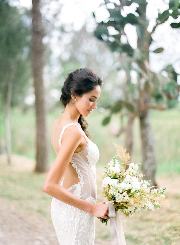 Side view portrait of bride wearing a Galia Lahav lace wedding gown adorned pearls and illusion paneling on the sides holding bouquet