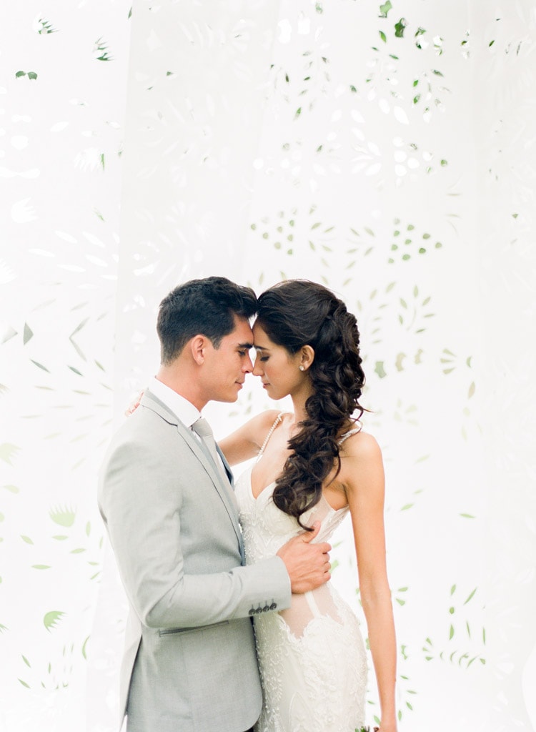 Married couple embracing each other touching foreheads with white perforated paper as the backdrop