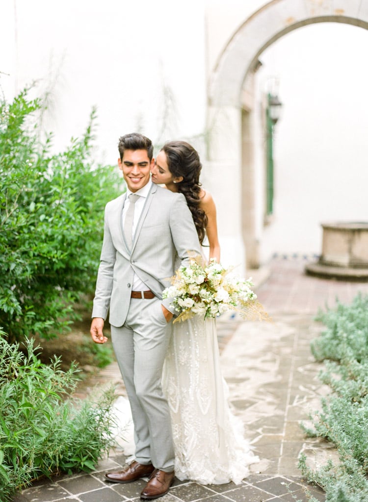 Walking around hacienda courtyard with bride behind groom about to give kiss on the cheek