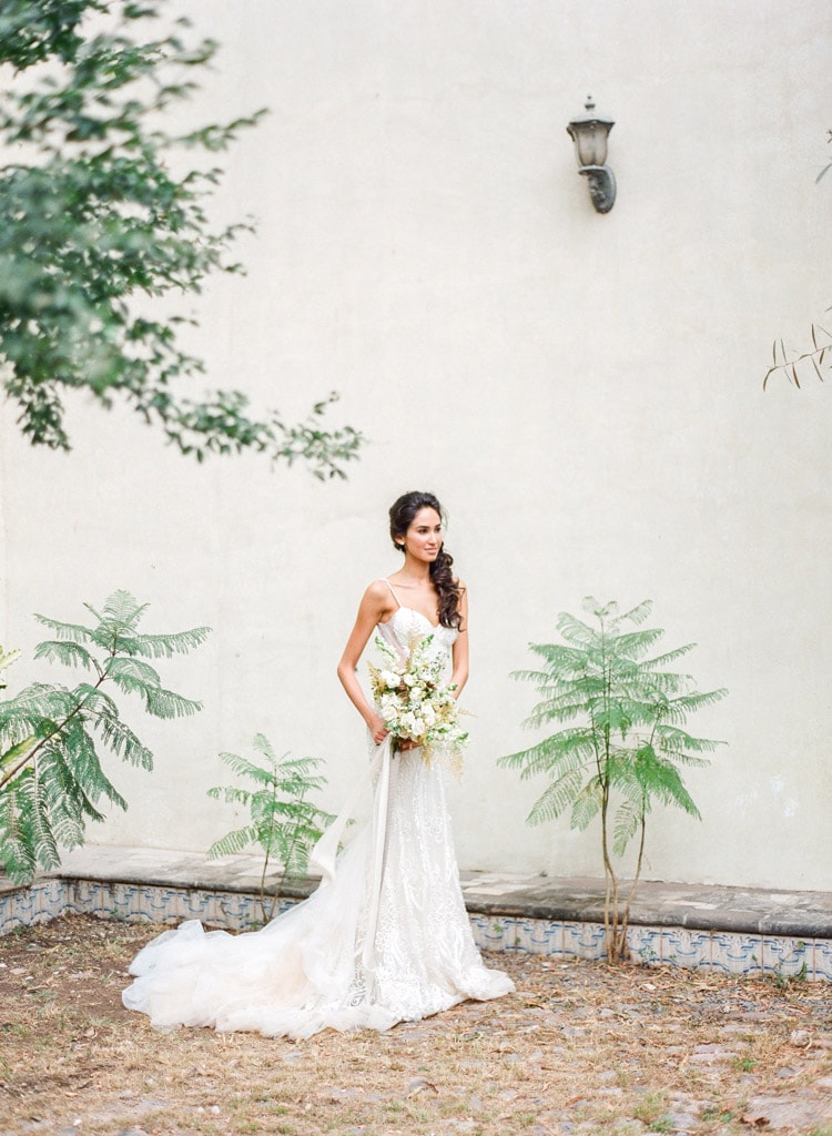 Bride surrounded by green vegetation with white wall as the backdrop