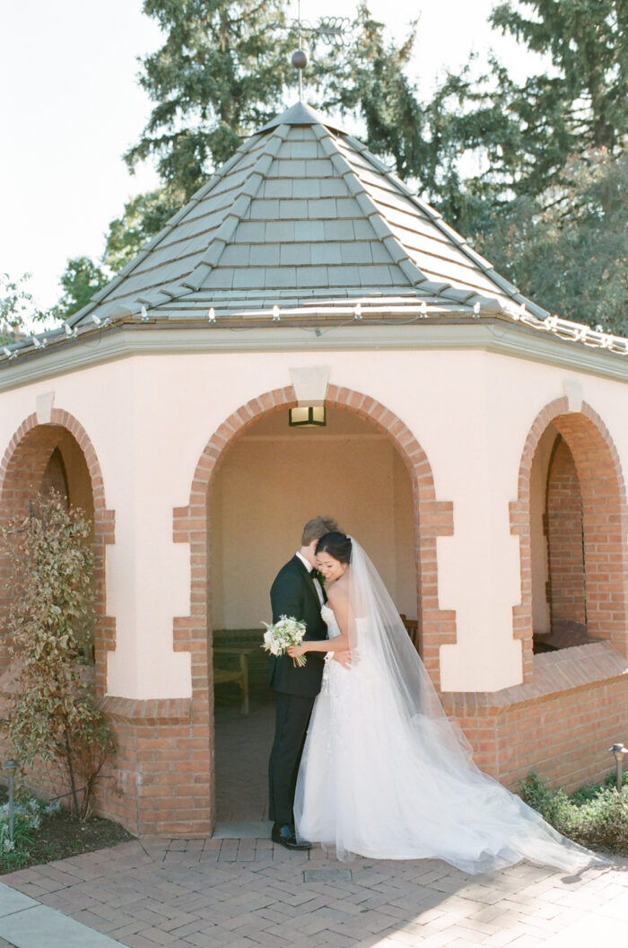 Groom and bride embracing in front of building with archway entrance