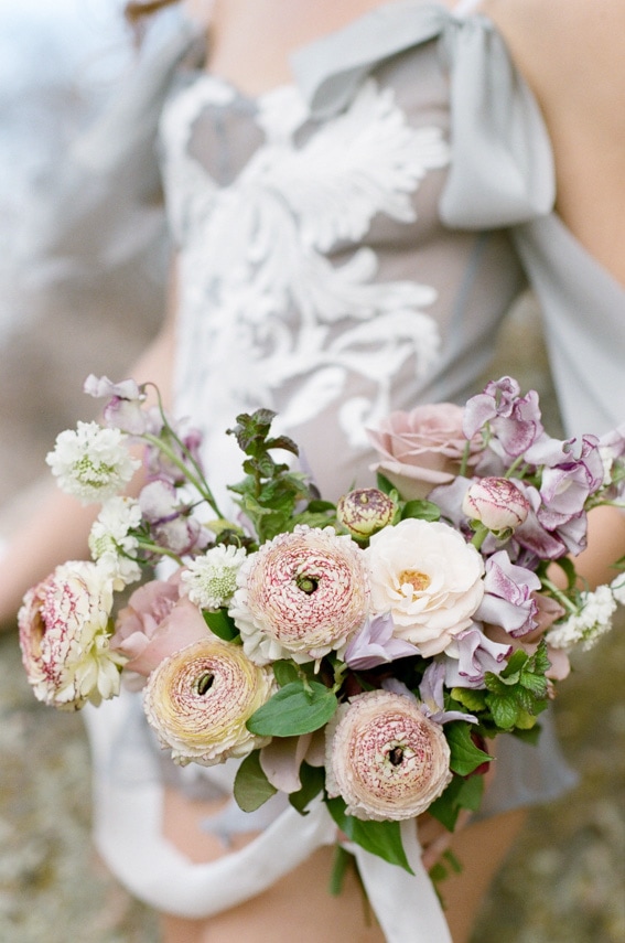 Bride wearing sophisticated French grey lingerie and holding a bouquet of flowers during bridal boudoir portraits in CO