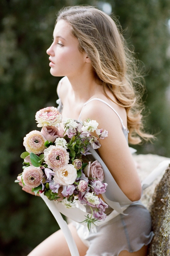 Bride wearing sophisticated French grey lingerie and holding a bouquet of flowers during bridal boudoir portraits