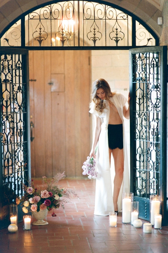 Bride wearing high-waisted black shorts and an elegant see-through white robe during boudoir portrait session