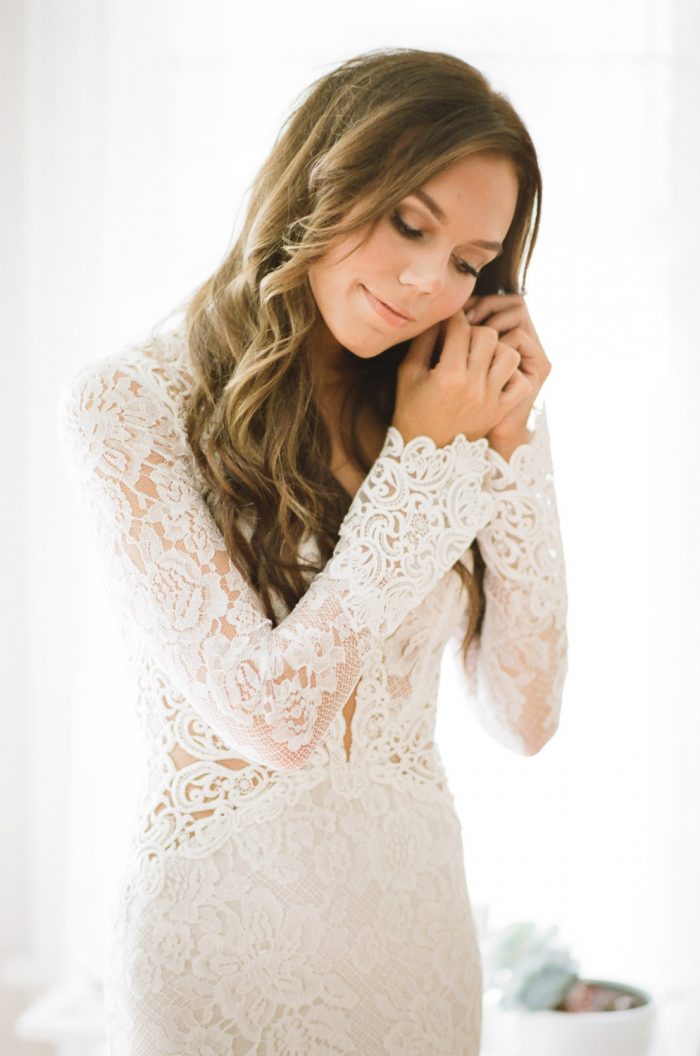 Bride in a Berta Bridal lace gown putting on her earrings on her Chicago wedding day