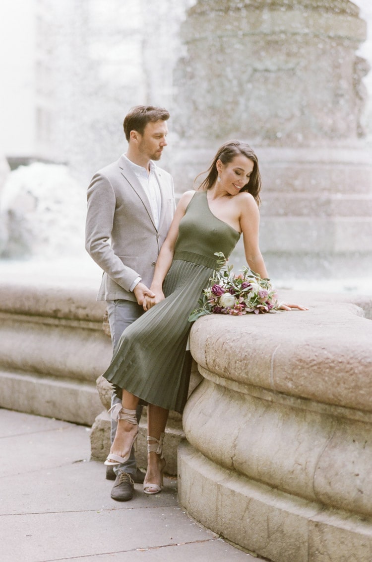 Couple sitting on a fountain in Munich during their engagement portrait session