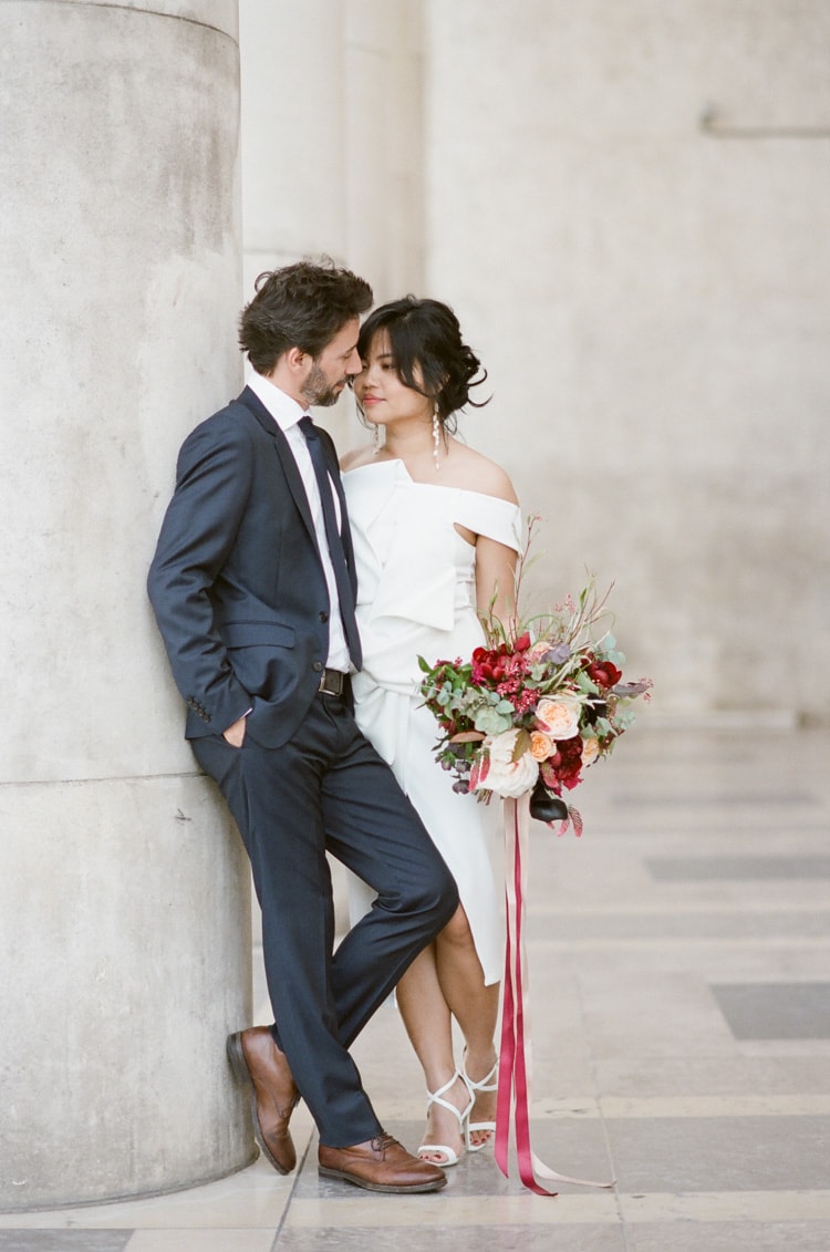 Romantic engagement session leaning against column with woman holding a large bouquet