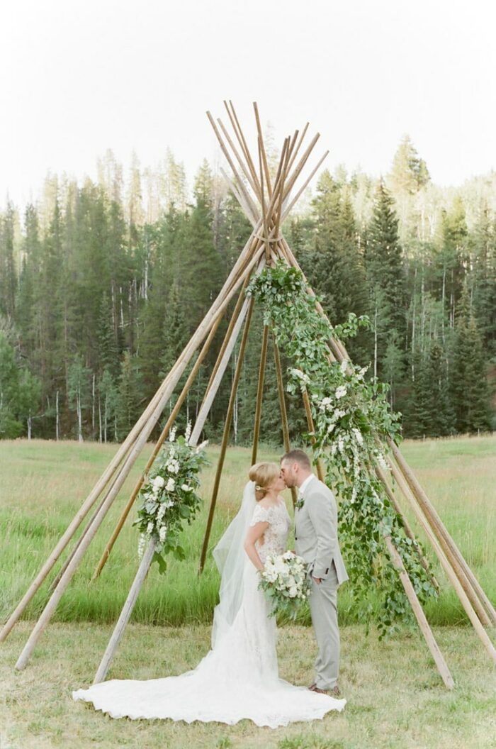 Couple kissing beneath a teepee structure at an outdoor wedding in Vail Colorado at Eaton Ranch