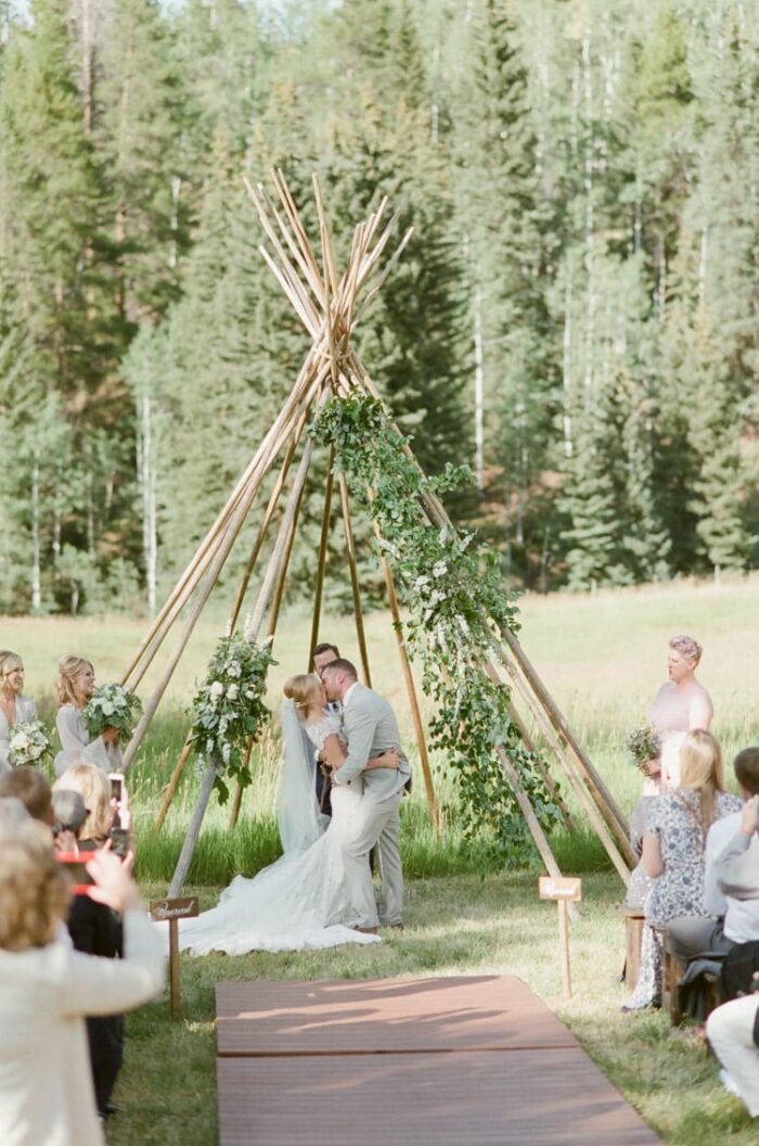 Couple kissing beneath a teepee structure at an outdoor wedding in Vail Colorado at Eaton Ranch