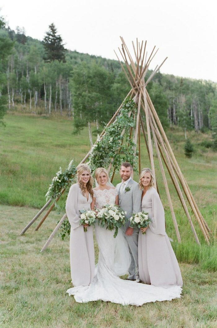 Wedding party standing in front of a teepee frame accented with floral