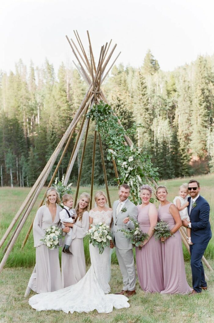 Wedding party standing in front of a teepee frame accented with floral