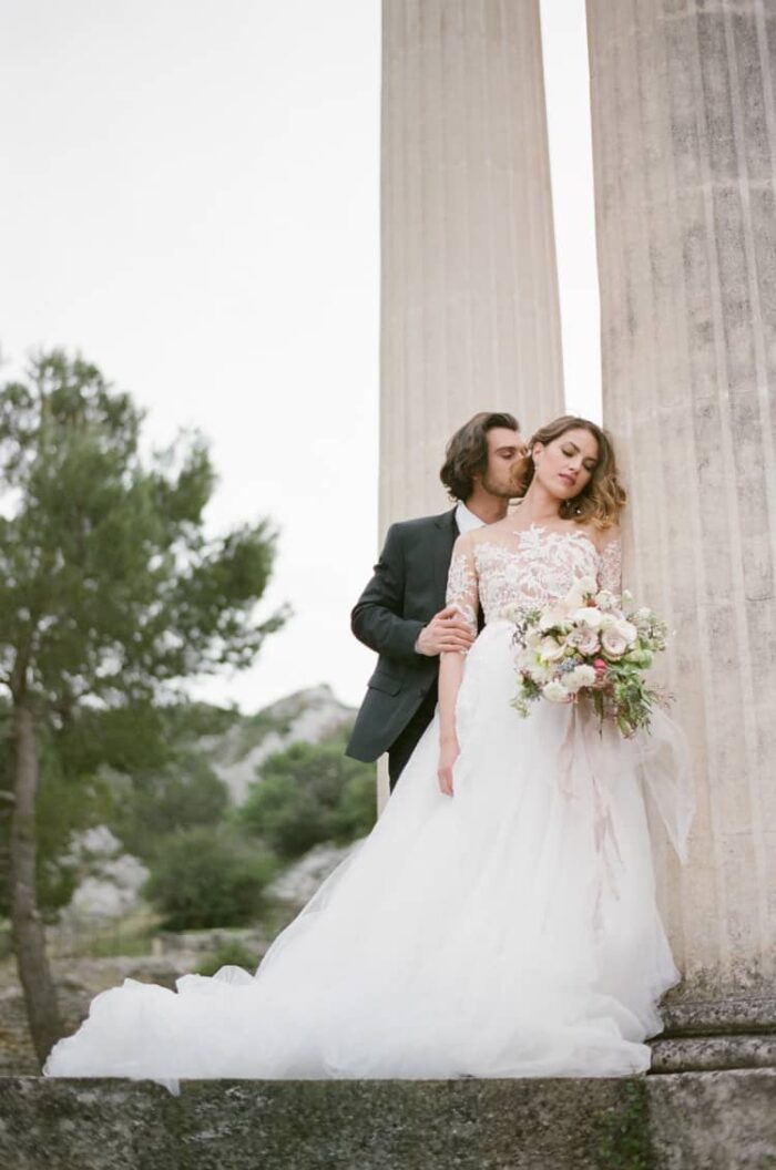 Bride and groom embracing each other next to a Roman column at the ruins of Glanum in Provence