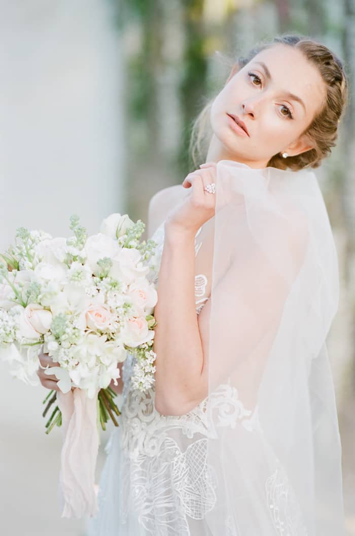 Bride posing in wedding dress with large bouquet of white flowers