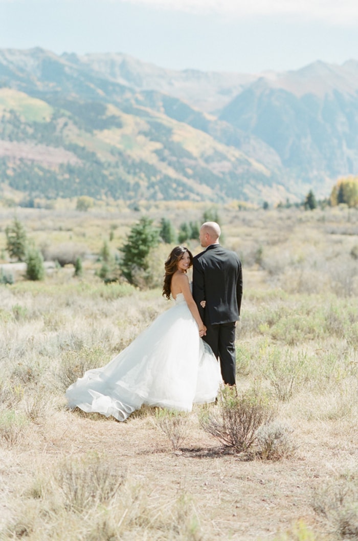 Engaged couple's backs turned looking at landscape of the Colorado mountains in Telluride