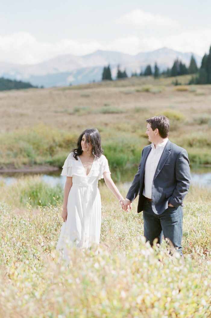 Couple holding hands and walking in tall glass with small body of water behind them