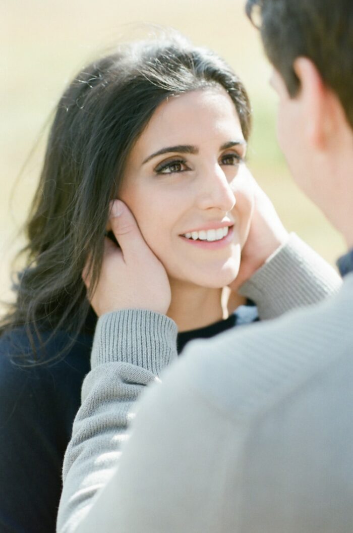 Fiance putting hands on sides of fiancee's face while she is smiling