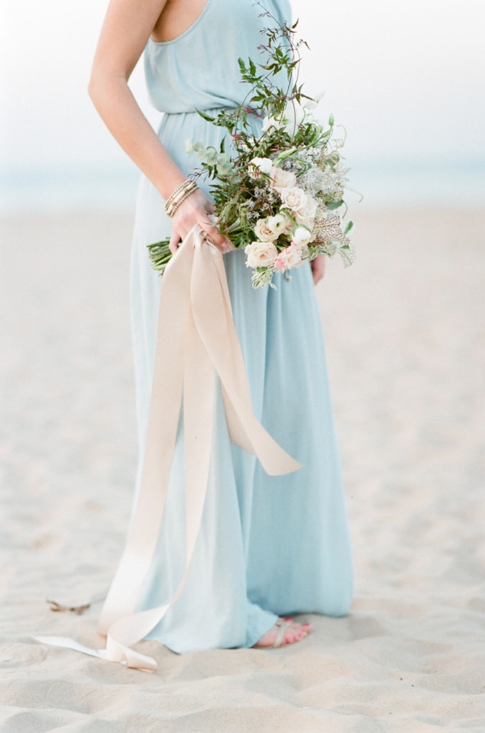 Engagement session centered on woman holding bouquet of flowers at the beach