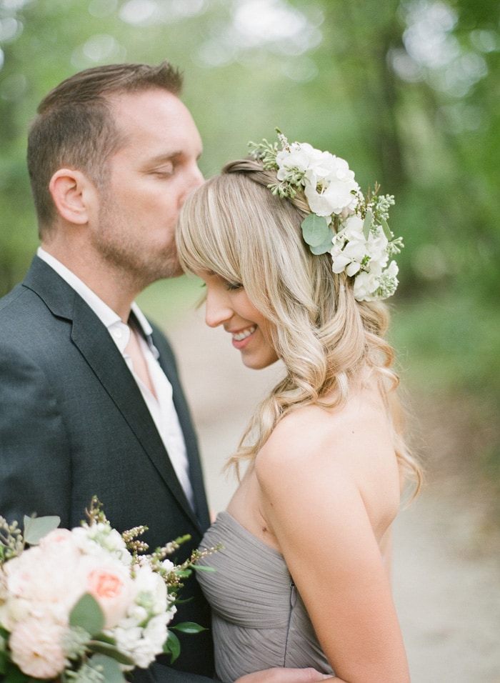 Bride-to-be with white flowers in hair and bouquet and groom-to-be kissing her