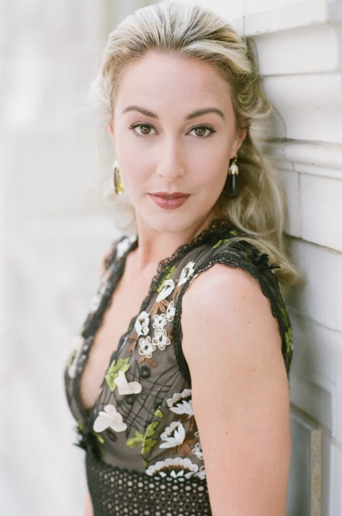 Woman wearing black mini dress with colorful floral embroidery up against stone white wall