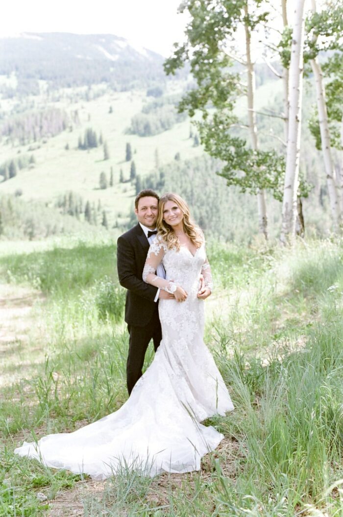 Groom embracing bride from behind outside in open grass fields