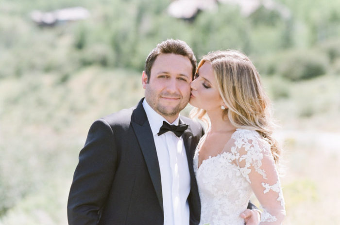 Bride kissing cheek of groom in open fields of grass