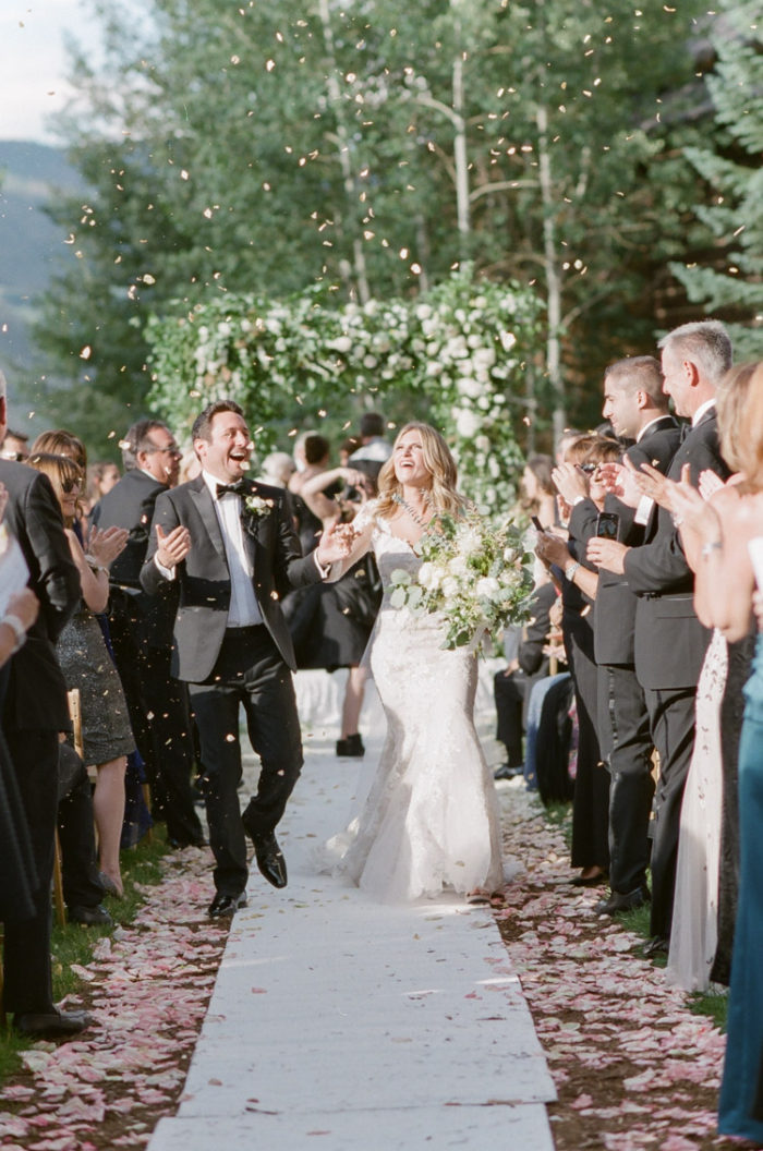 Happy couple walking down the aisle with flower petals in the air