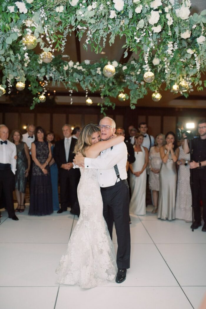 Bride slow dancing with father with huge floral halo above white dance floor