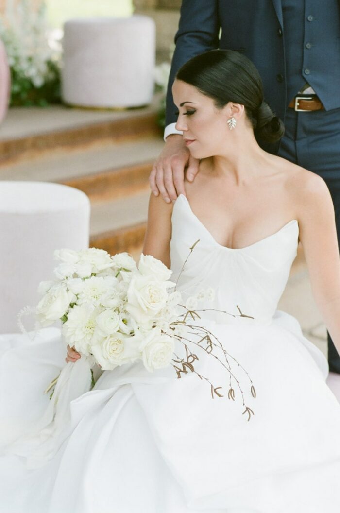 Bride sitting holding white bouquet in white wedding dress