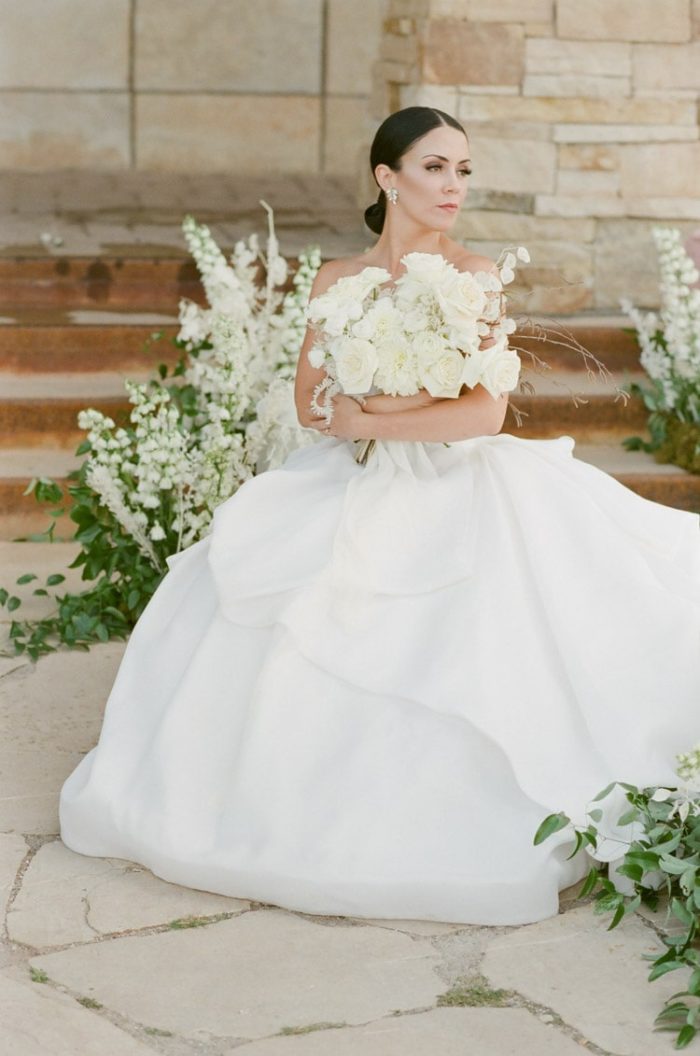 Bride sitting down bidding holding bouquet in arms with large white skirt