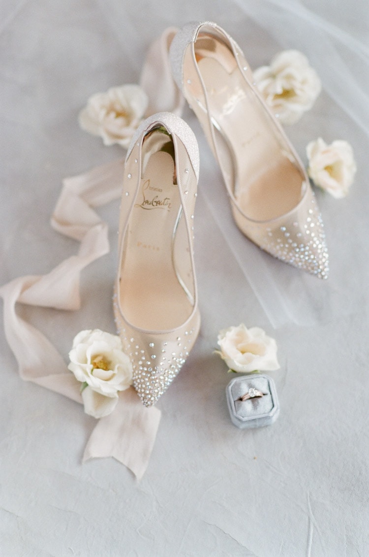 Detailed shot of sparkly Louboutin shoes surrounded by white flowers and wedding ring