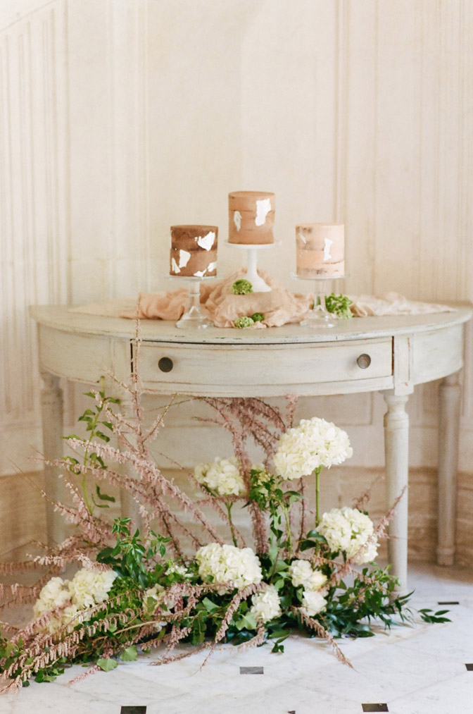 White table against wall with candles and greenery with white flowers below