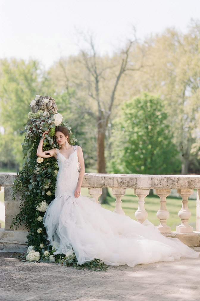 Bride leaning against decorated greenery outside