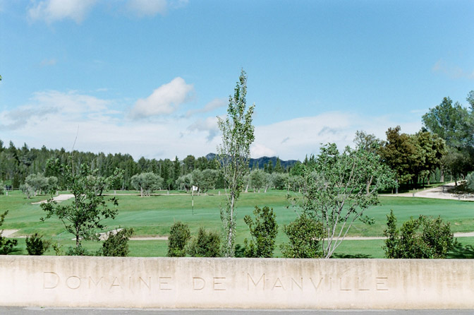 Engraving in stone that says Domaine de Manville with golf course behind it