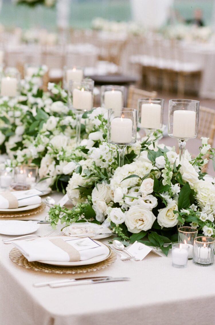 Row of white flower arrangements and candles on table