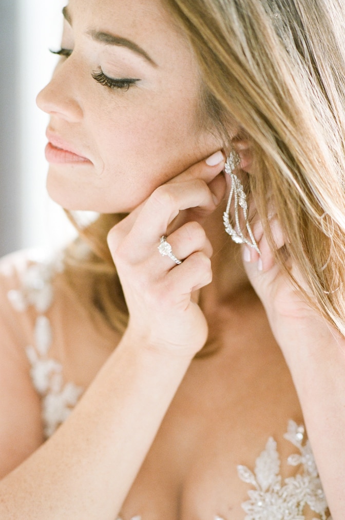 Closeup of a bride putting her earrings on while wearing a luxury expensive designer engagement ring by Tiffany & Co