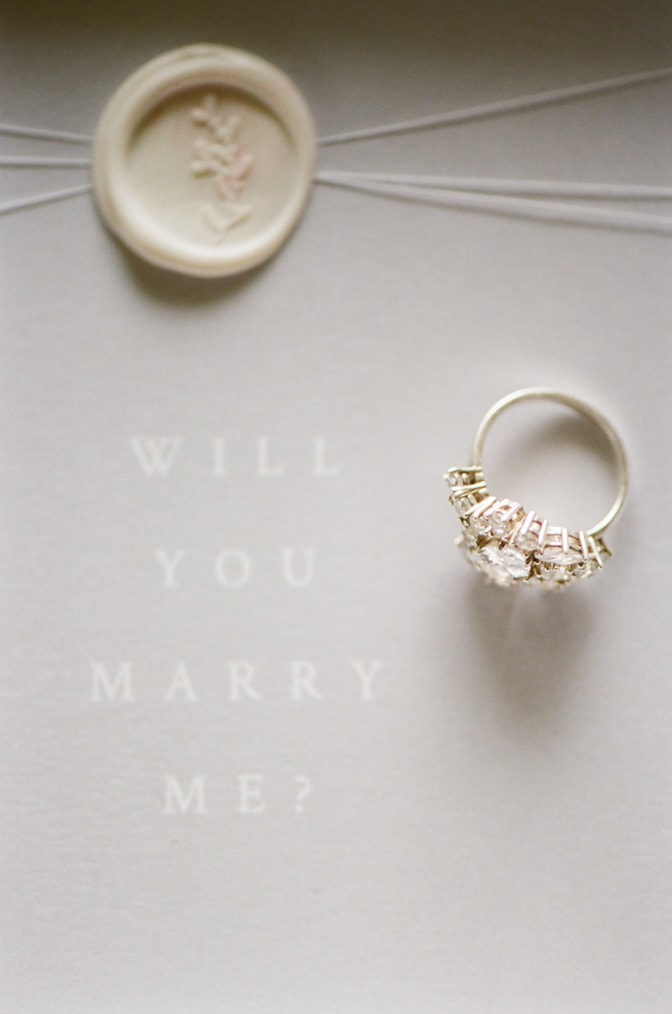 Luxury designer engagement ring by Susie Saltzman placed on an invitation sign saying 'Will you marry me?"