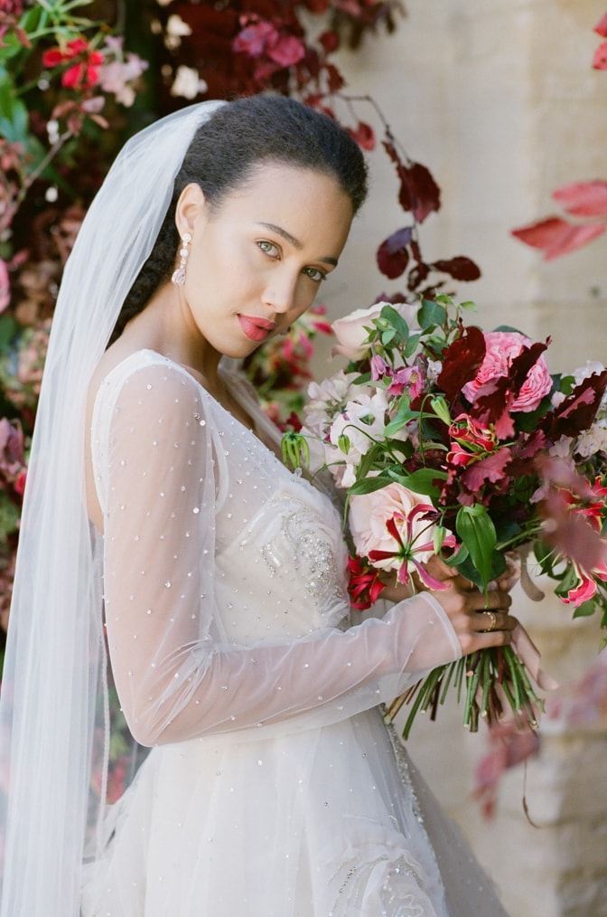Closeup of a black bride in her blush Inbal Dror wedding gown holding her colorful bouquet at Chateau Martinay