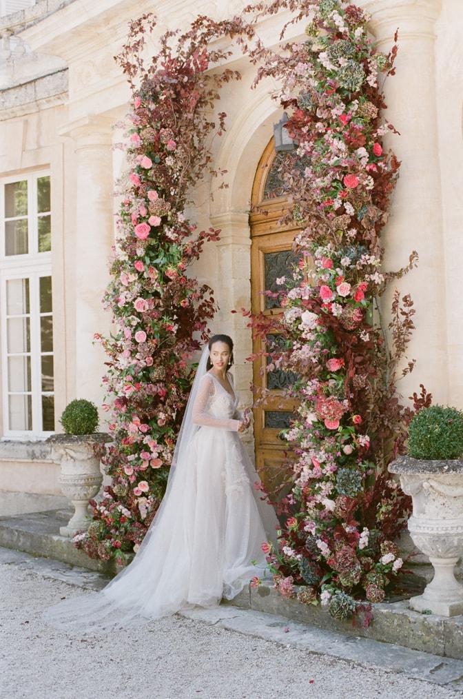 Bride standing under her flower wedding arch in front of Chateau Martinay in Provence