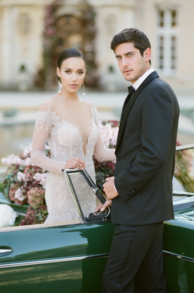 Bride and groom standing in front of a green car filled with hydrangea and looking into the camera at Chateau Martinay Provence