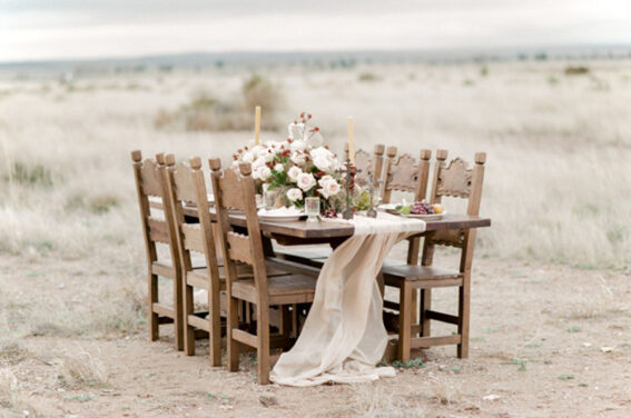 Wedding table showcasing blush silk table runner and colorful floral centerpieces surrounded by six chairs