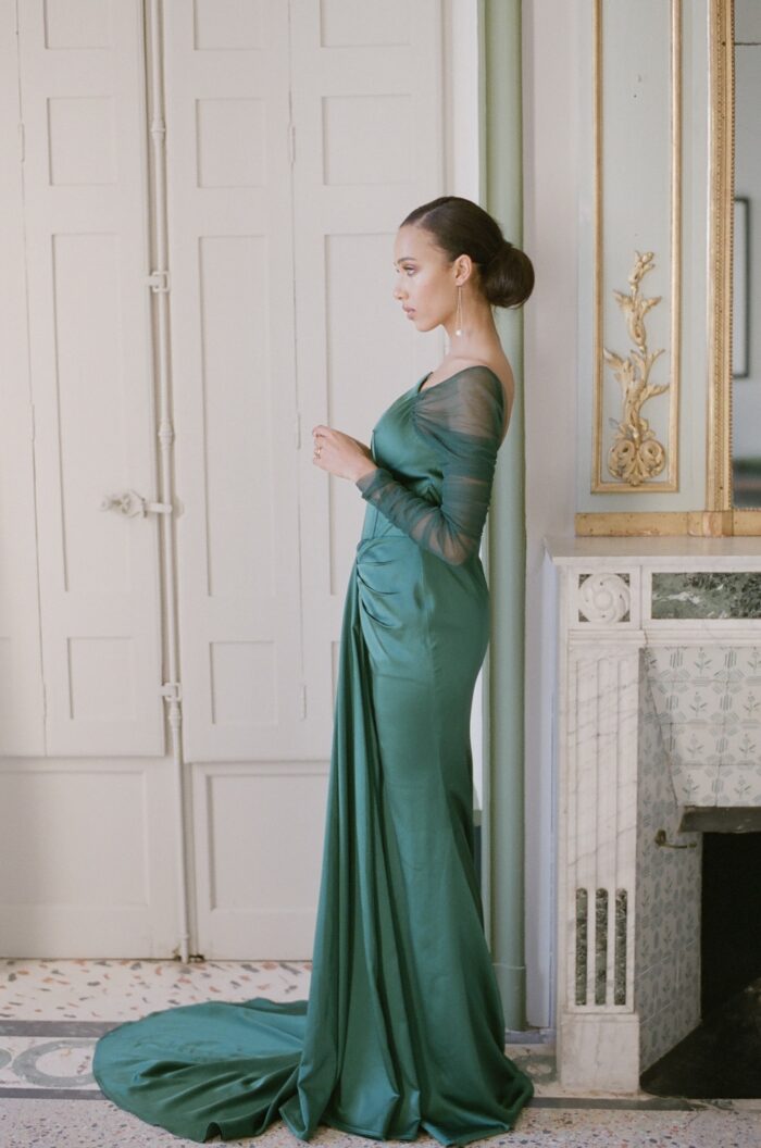 Bride in green dress leaning on wall of fireplace