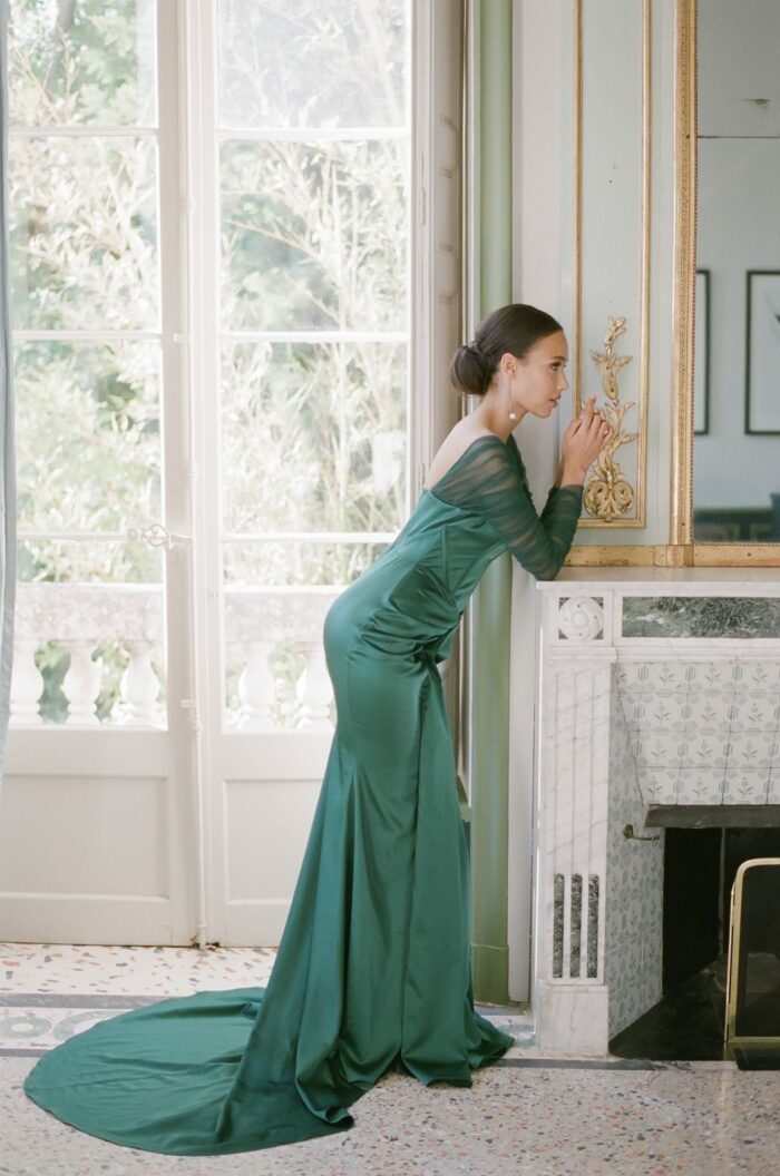 Bride in green dress leaning on fireplace at castle