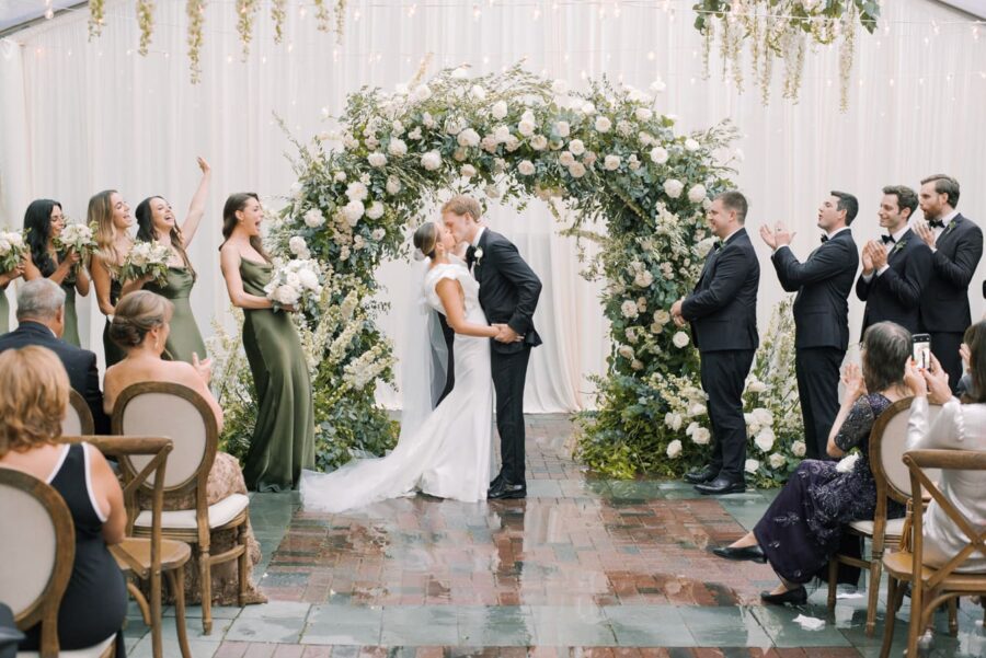 Bride and groom kissing each other under floral wedding arch after saying 'yes'