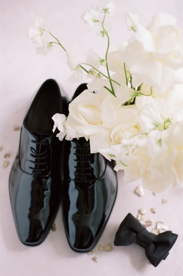 Groom's glossy shoes placed next to bow tie