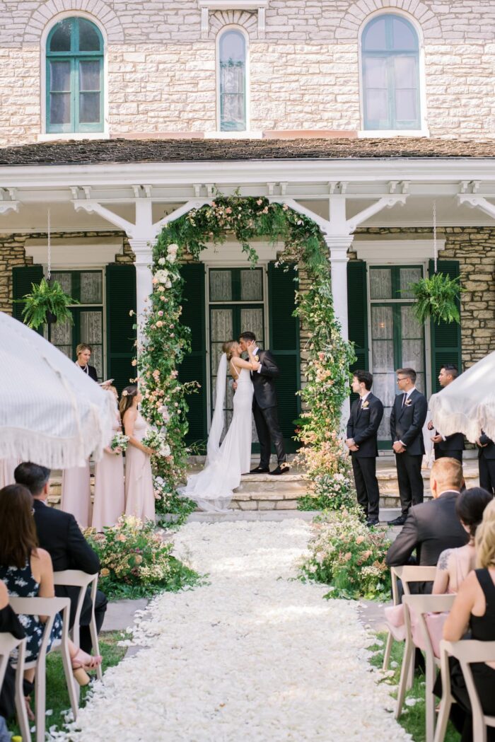 Bride and groom kissing each other under floral arch at Oakland House