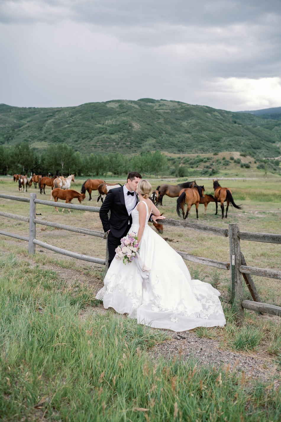 Bride and groom kissing in front of horses and mountains in Aspen