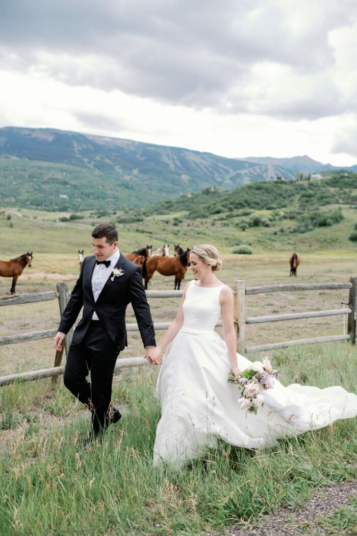 Bride and groom walking in front of horses and mountains in Aspen